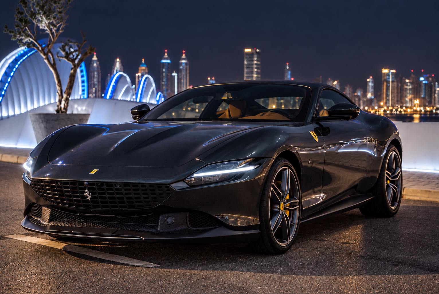 Dark grey grand-touring coupe parked beside a lit waterfront bridge at night, the Dubai skyline glowing behind